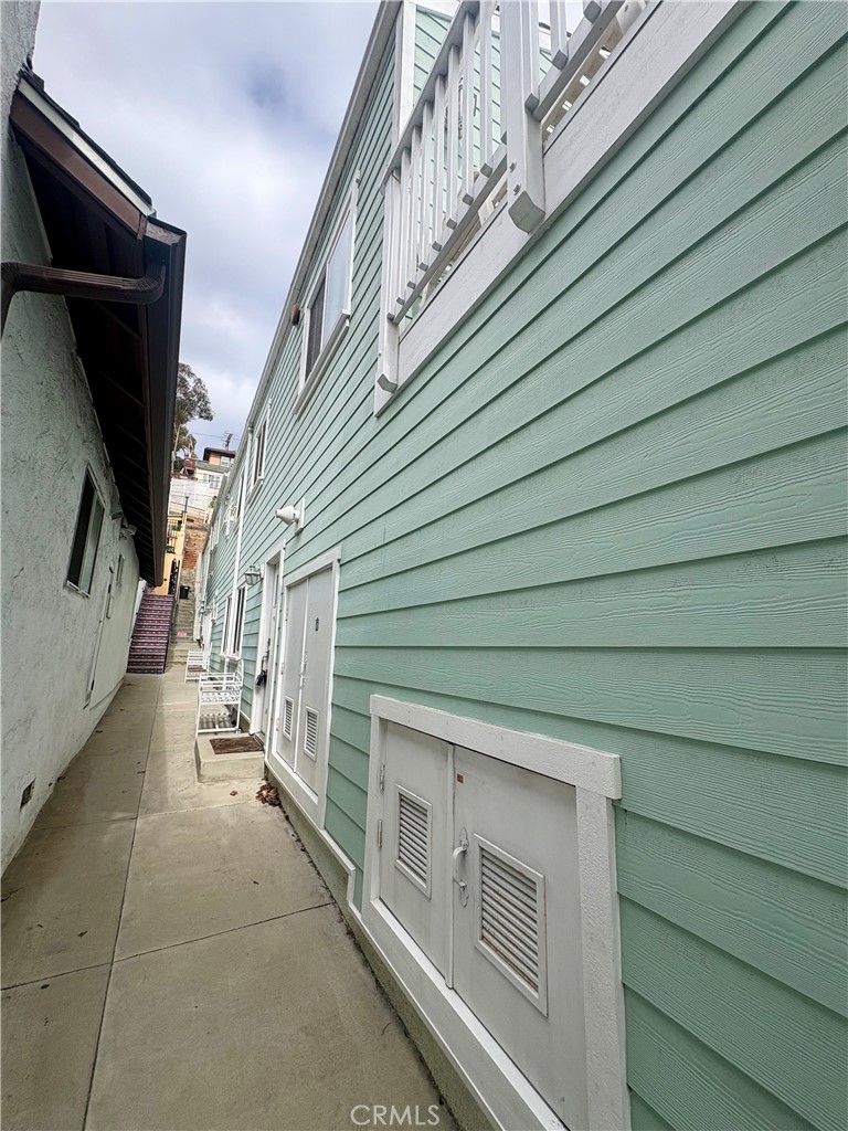 Side walkway beside a mint-green home, with white utility doors and stairs at the far end.