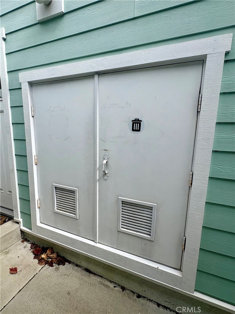 Gray double-door utility enclosure with ventilation grilles set into aqua siding.