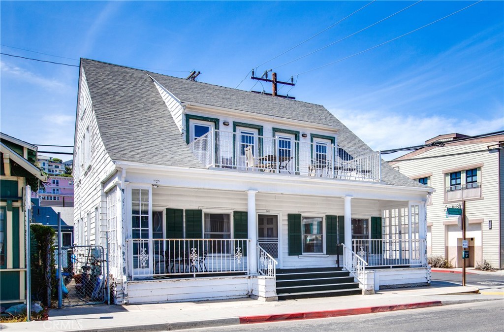 White two-story house with green shutters, a second-floor balcony, and a covered front porch.