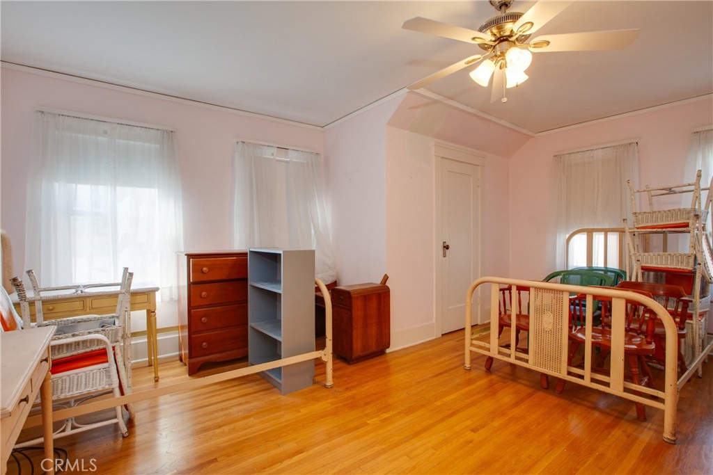 Bedroom with a wooden crib, hardwood floors, pink walls, and a ceiling fan.