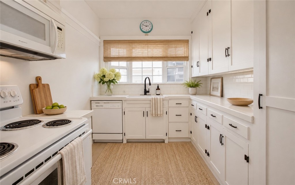White kitchen with shaker cabinets, a black faucet, and a woven window shade.