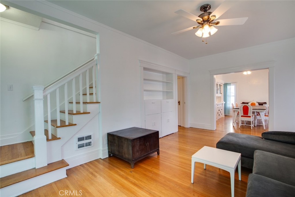 Living room with hardwood floors, a white staircase, built-in shelving, and a dining area beyond.