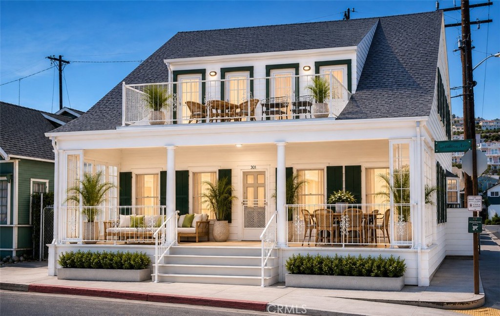 White two-story house with green shutters, a furnished wraparound porch, and an upper balcony.