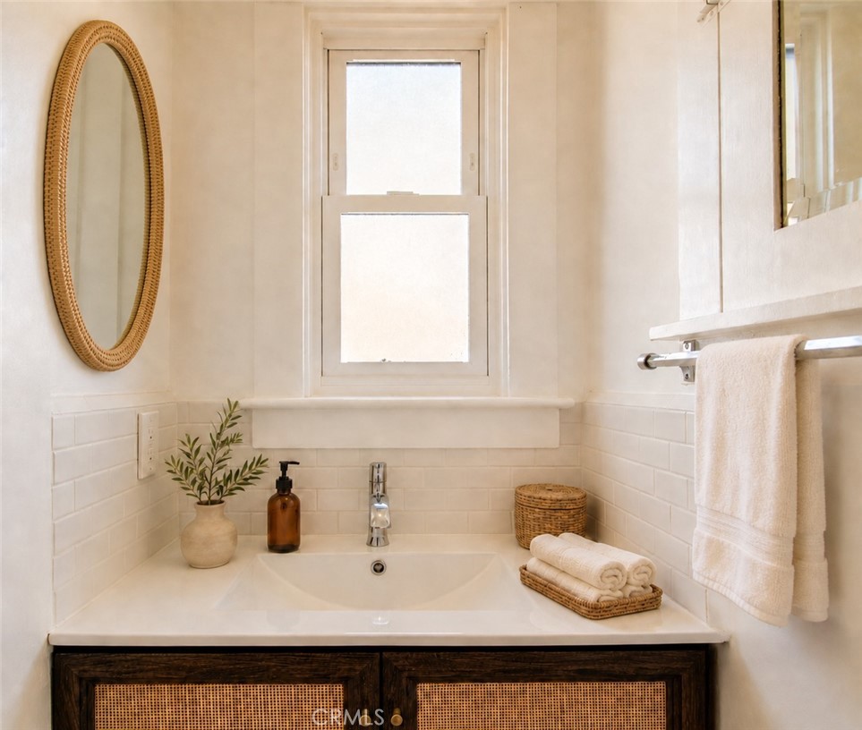 Bathroom vanity with a white sink, dark woven-front cabinetry, and an oval rattan-framed mirror.