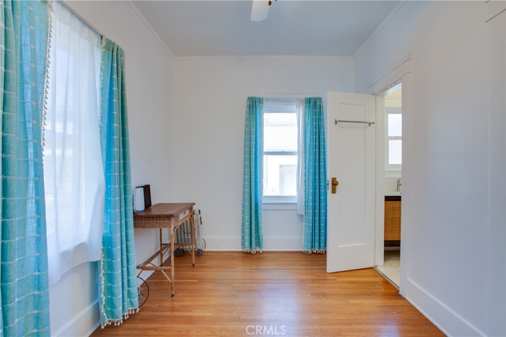 Room with hardwood floors, turquoise curtains, two windows, and an open bathroom door.