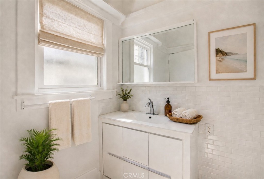 Bright bathroom with a white vanity, large mirror, shaded window, and subway tile.