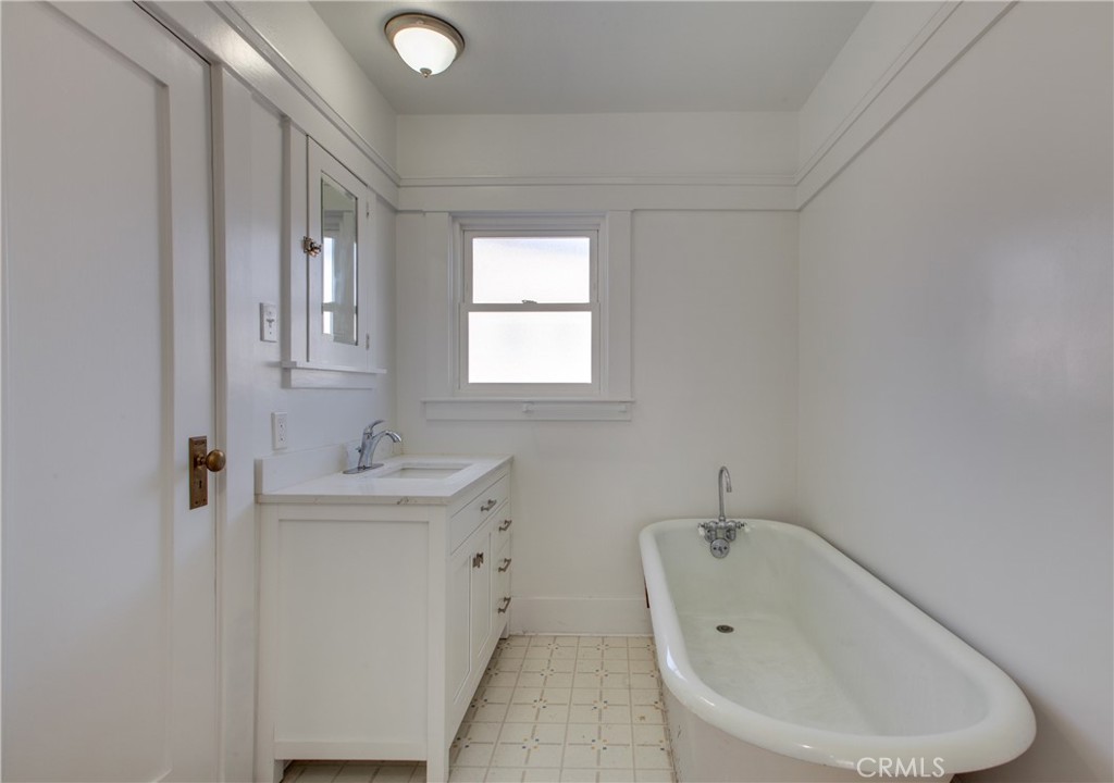 Bathroom with a freestanding vintage-style tub, white vanity, and patterned tile floor.