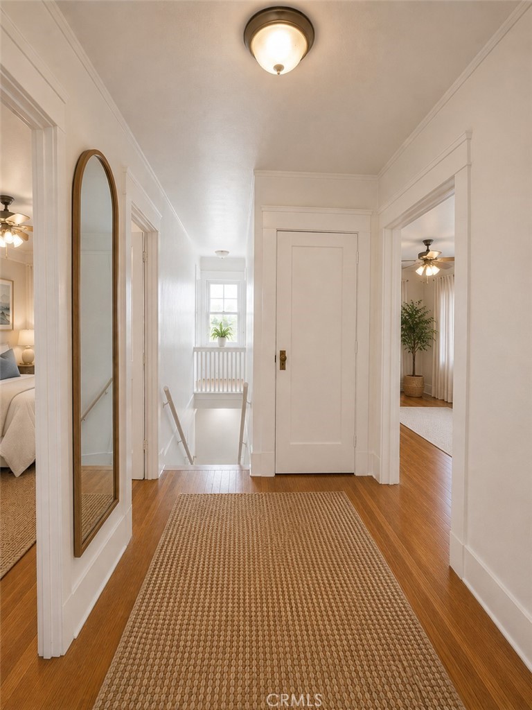 Bright hallway with warm wood floors, a woven runner, arched mirror, and window overlooking the stairs.