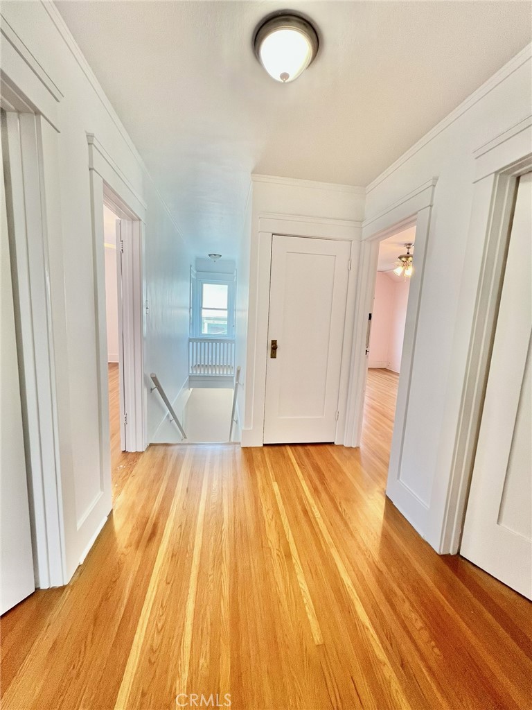 Hallway with polished hardwood floors, white paneled doors, and a stairwell at the end.
