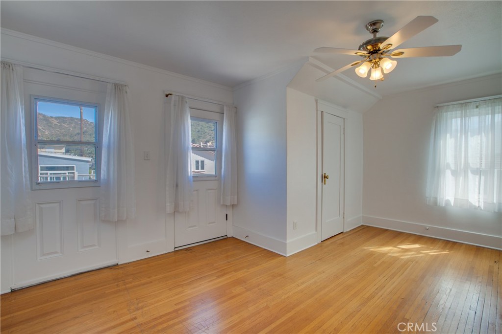 Vacant room with hardwood floors, white walls, a ceiling fan, and curtained windows.