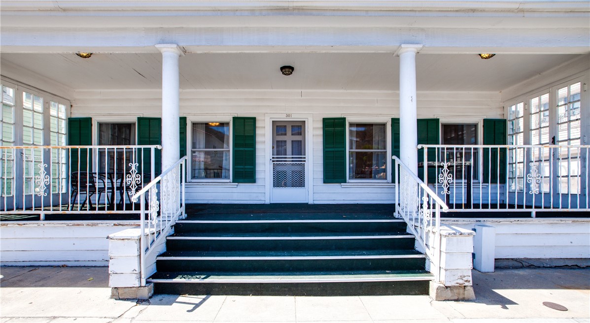 White house with green shutters and a covered porch, viewed from the front steps.