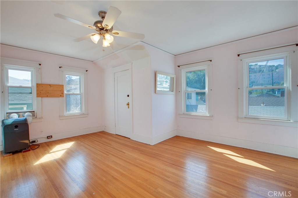 Vacant room with hardwood floors, a ceiling fan, and multiple windows.
