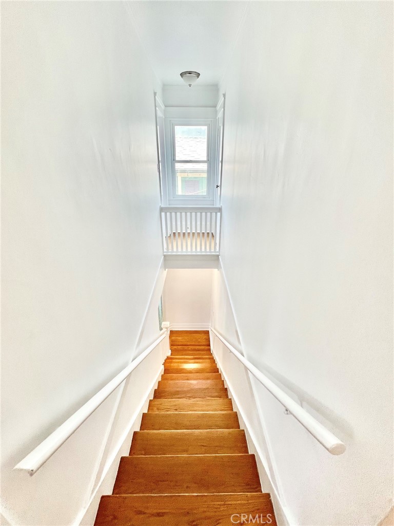 Narrow wooden staircase with white handrails leading down from a bright window at the landing.