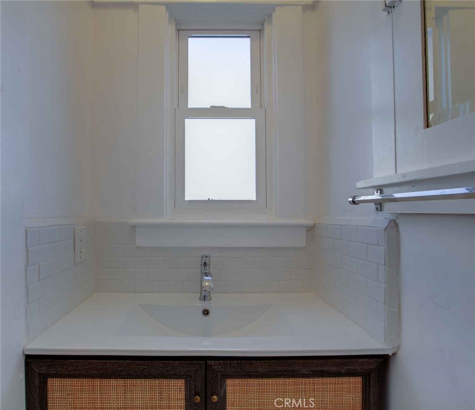 Bathroom vanity with a white sink, chrome faucet, cane-front cabinets, and a window above.