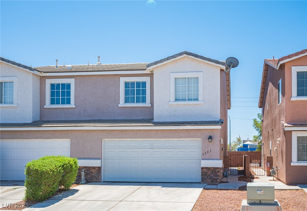 Two-story stucco home with a two-car garage, stone accents, and a front shrub.