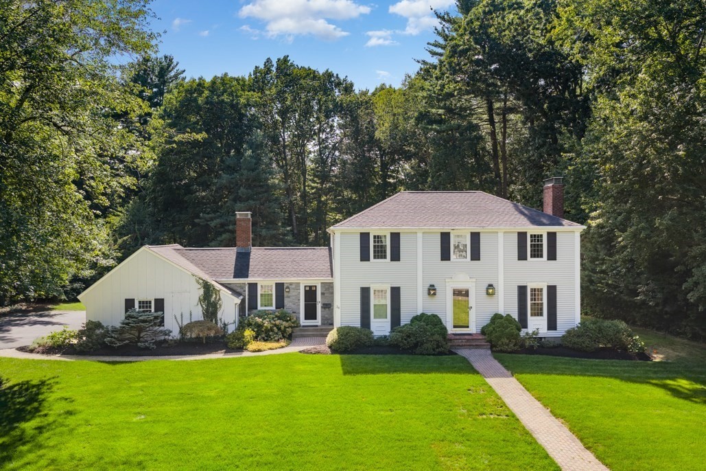 White two-story house with black shutters, attached wing, and brick walkway across a green lawn.