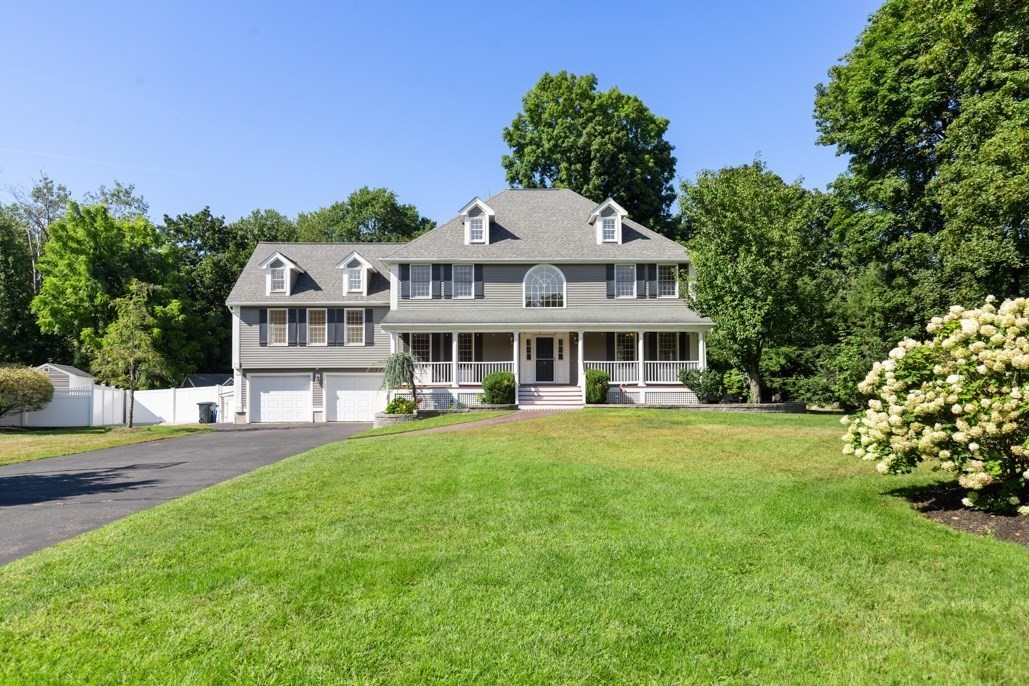 Gray two-story home with dormers, a covered porch, and attached garage beyond a broad green lawn.