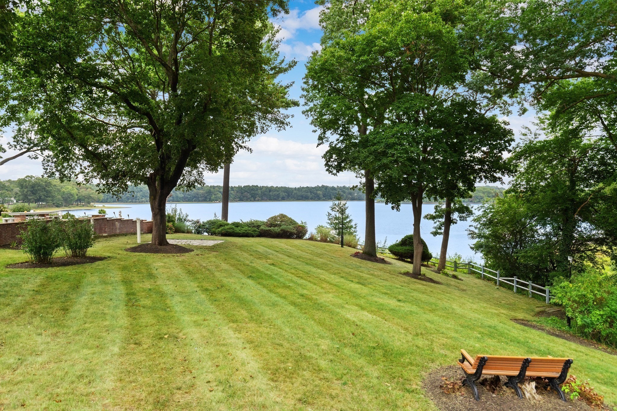 Tree-shaded lawn and wooden bench overlooking a lake in Lynnfield.