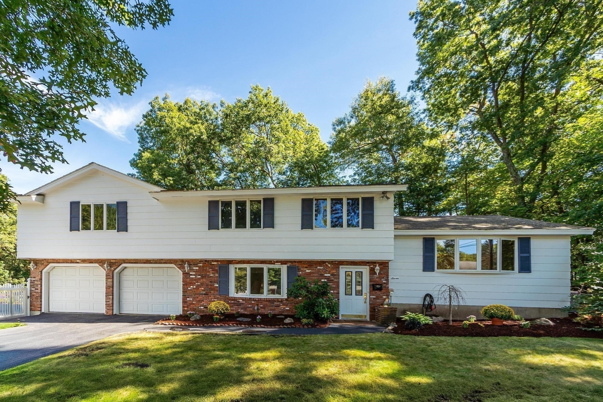 Split-level home with white siding, brick lower facade, two-car garage, and leafy trees.