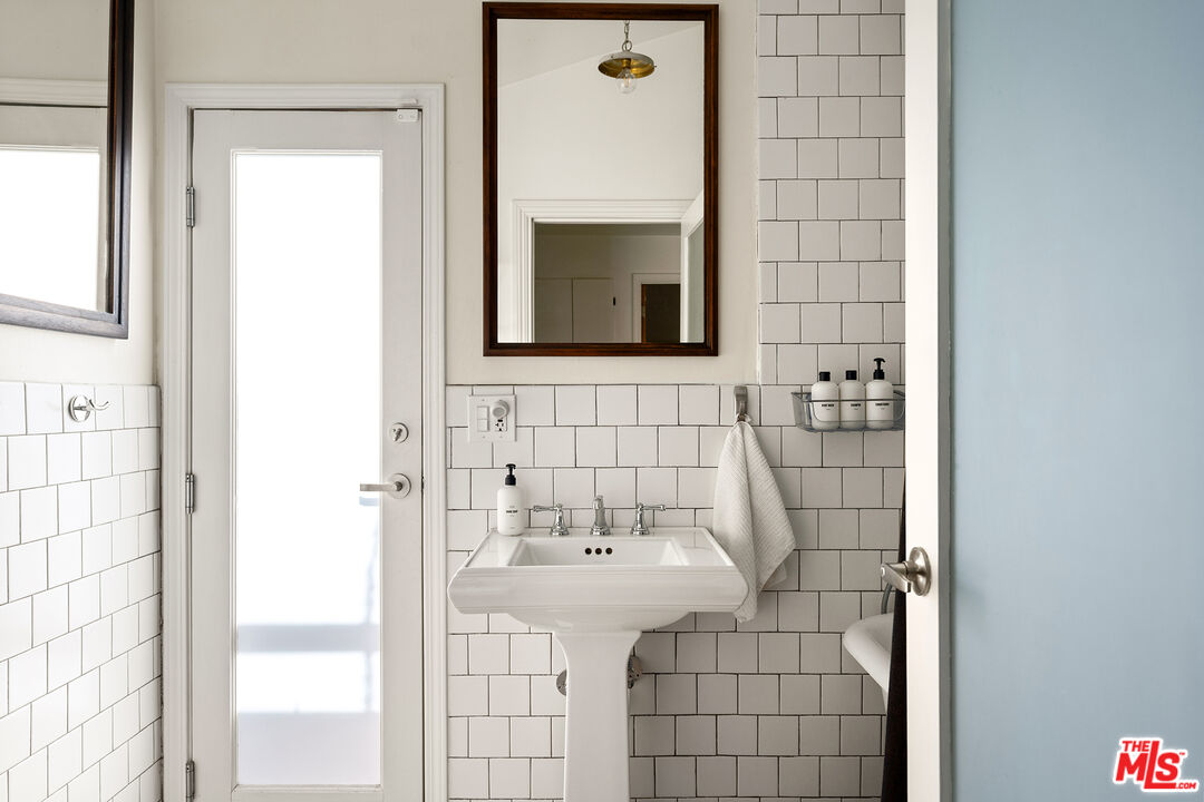 Bathroom with a pedestal sink, dark-grouted subway tile, and a framed mirror.