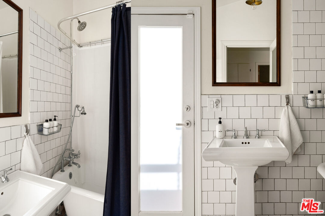 Bathroom with white subway tile, a pedestal sink, and a bathtub behind a dark curtain.