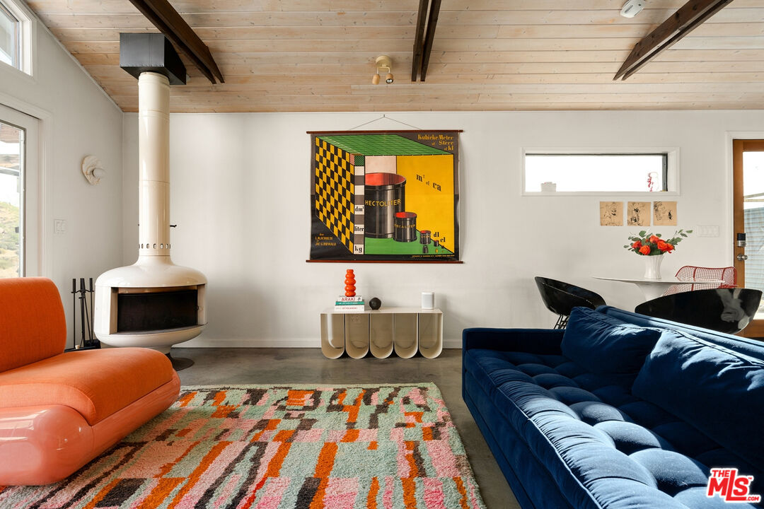 Living room with a white freestanding fireplace, colorful geometric rug, and exposed ceiling beams.