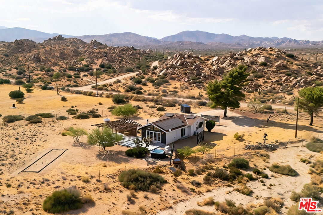 Desert home with rooftop solar panels and a covered patio amid rocky hills.