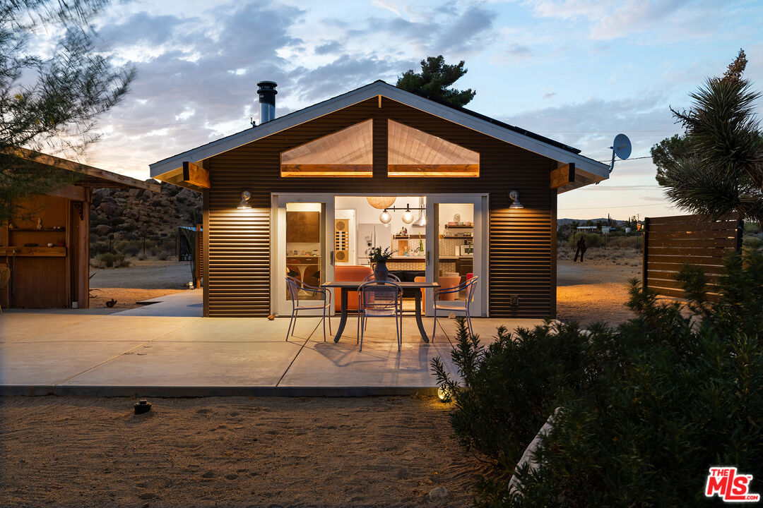 Modern desert home at dusk, with a glowing interior and outdoor dining patio.