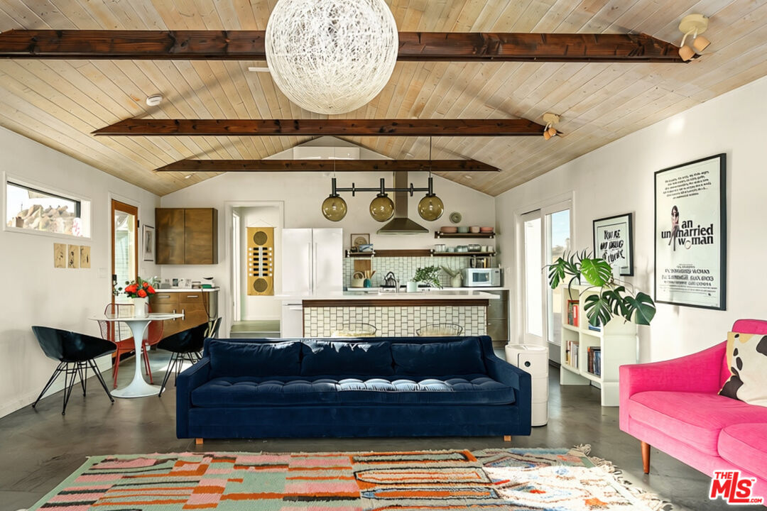 Open-plan living room with a vaulted wood ceiling, exposed beams, navy sofa, and bright pink chair.