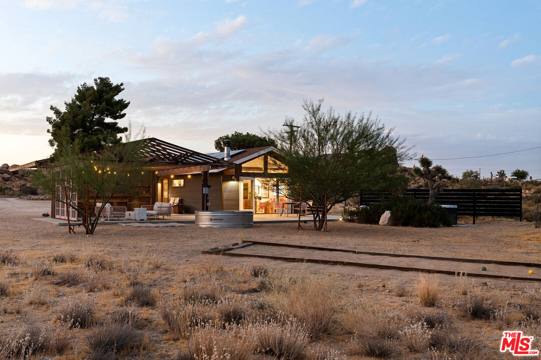Desert home at dusk with a covered patio, warm lights, and a circular stock-tank pool.