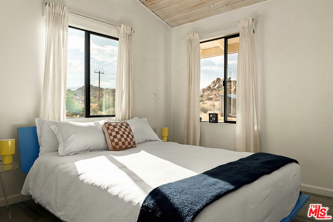 Bedroom with a white bed and curtained windows overlooking rocky desert hills.