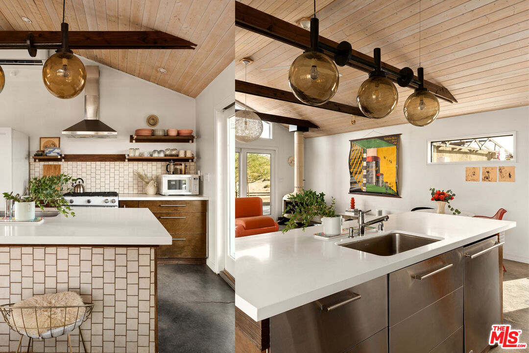 Kitchen with a large white island, stainless-steel sink, and vaulted wood-plank ceiling.