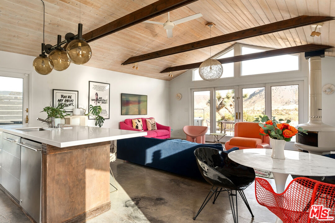 Open-plan living room and kitchen with exposed beams, colorful seating, and glass doors facing the desert.