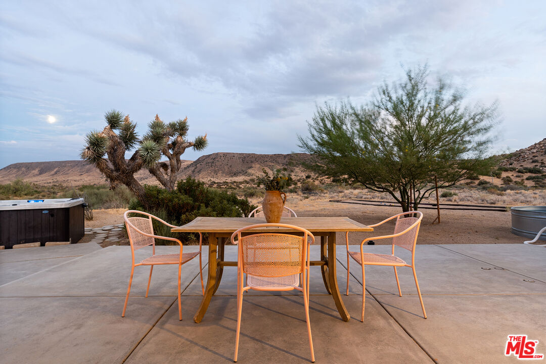 Outdoor dining patio with orange chairs, a hot tub, Joshua trees, and desert mountains.