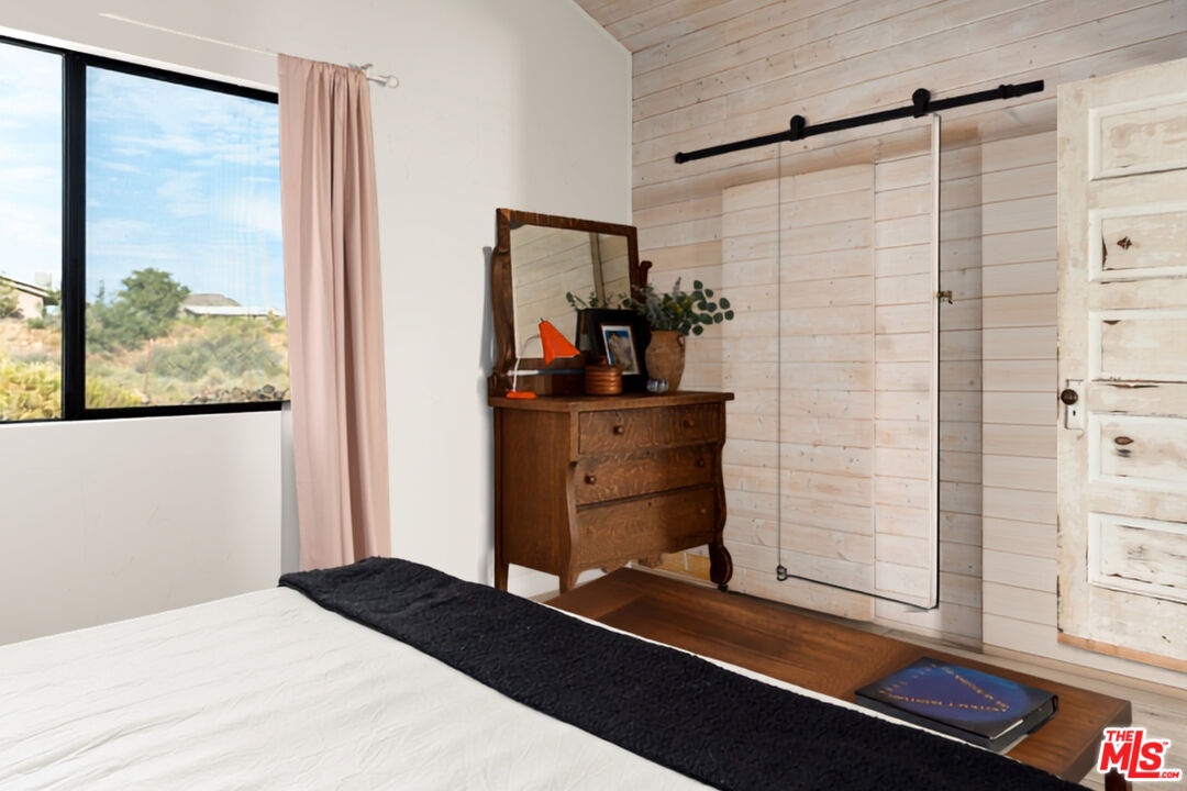 Bedroom with a large window, vintage wooden dresser, and sliding white plank door.