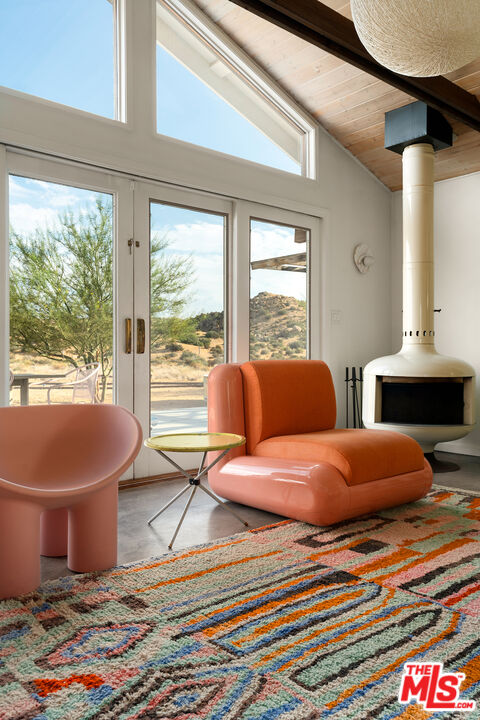 Living room with orange lounge chairs, vaulted wood ceiling, glass doors, and freestanding fireplace.