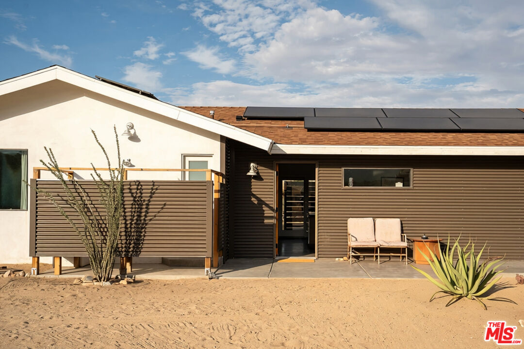 Modern desert home with rooftop solar panels and a screened patio with two chairs.