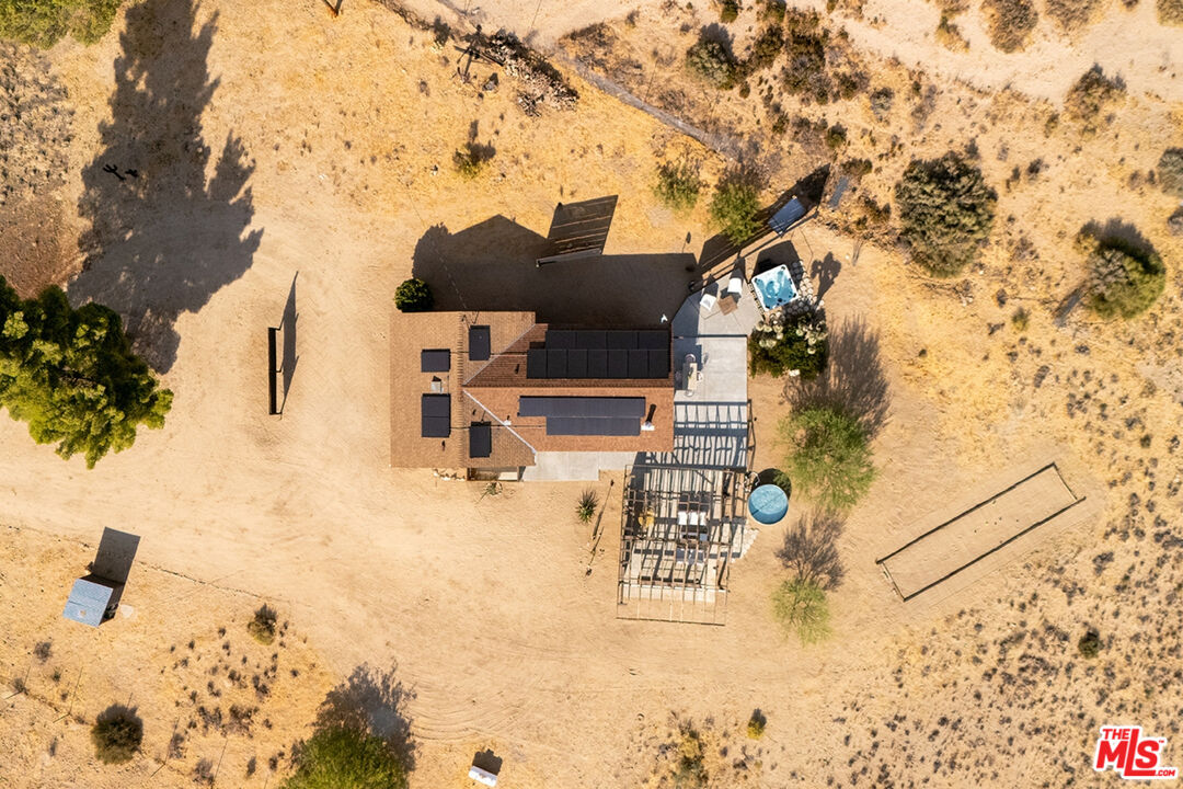 Desert home with rooftop solar panels, a pergola structure, and small outdoor pools on a sandy lot.