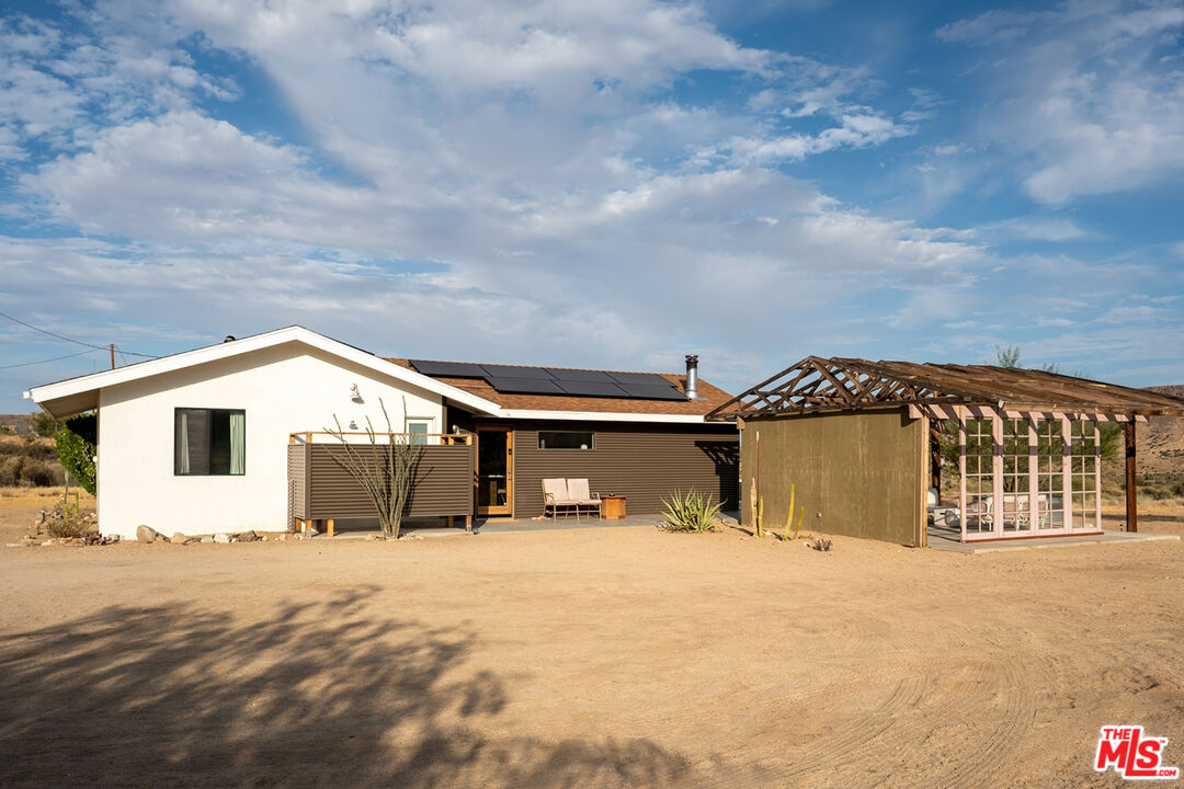 Single-story desert home with rooftop solar panels and an attached timber-frame structure.