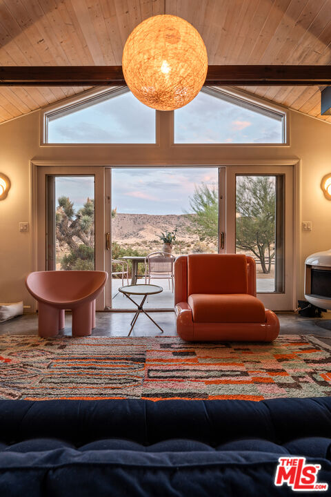 Living room with a vaulted wood ceiling, expansive glass doors, and desert hillside views.