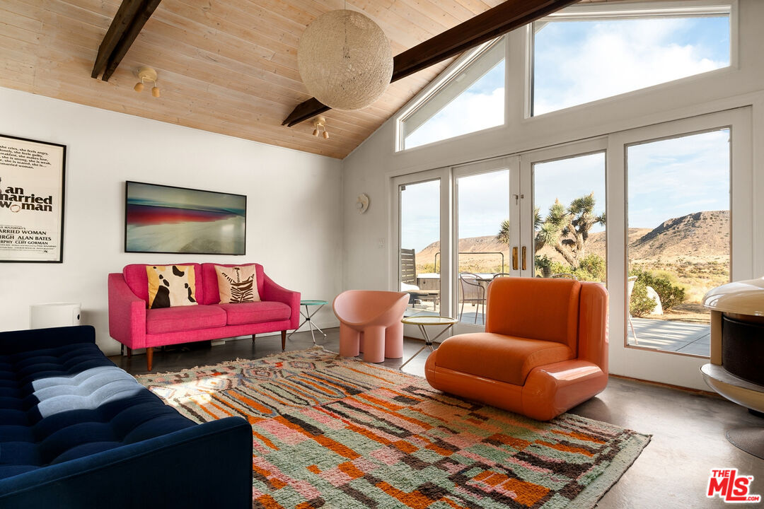 Living room with colorful seating, a vaulted wood ceiling, and large windows overlooking desert mountains.