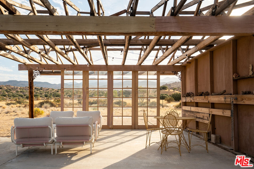 Covered patio with exposed timber roof framing, lounge chairs, and desert and mountain views.
