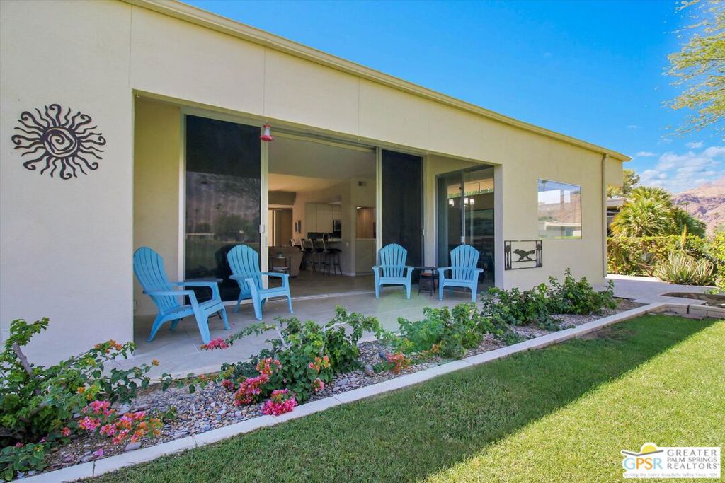 Modern home with wide glass doors, blue patio chairs, and a landscaped garden.