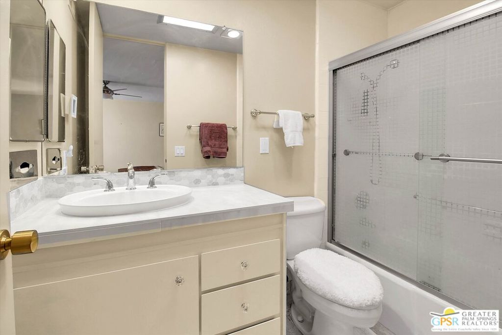 Bathroom with a cream vanity, oval sink, and glass-enclosed tub and shower.