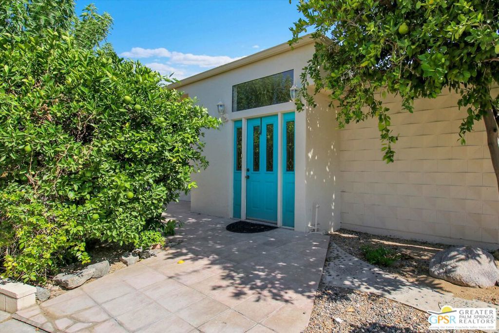 Home entrance with a bright turquoise door, paved walkway, and leafy landscaping.