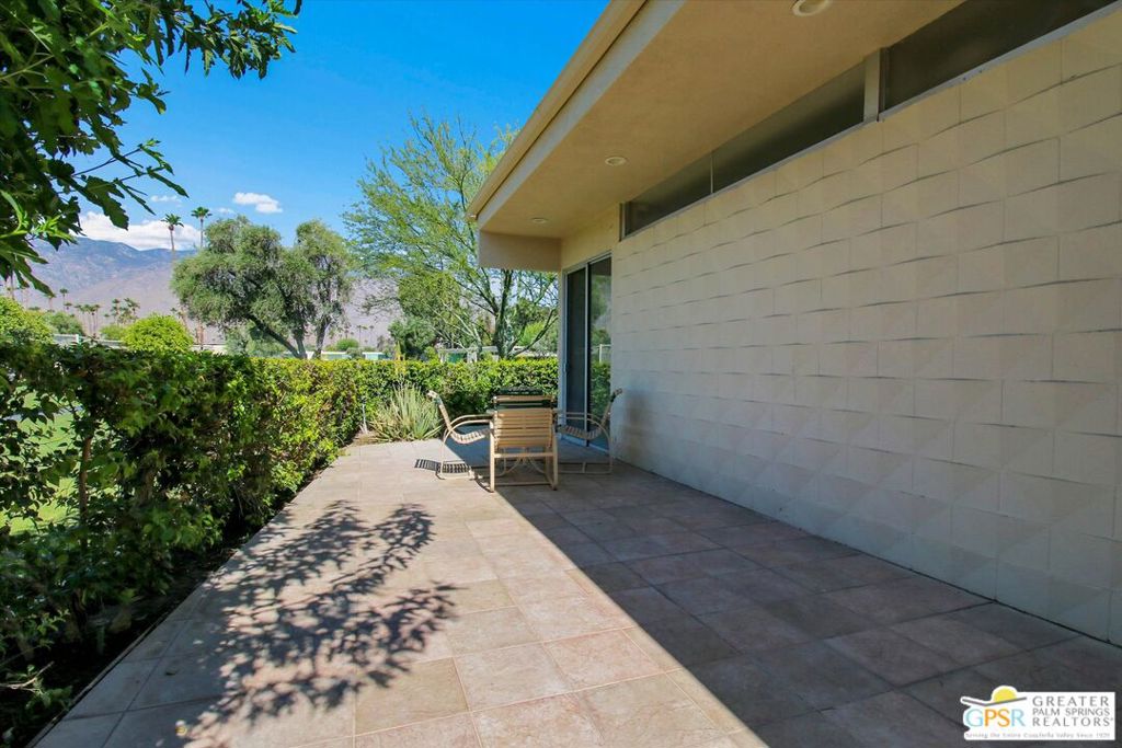 Paved patio with two chairs beside a modern home, overlooking trees and distant mountains.