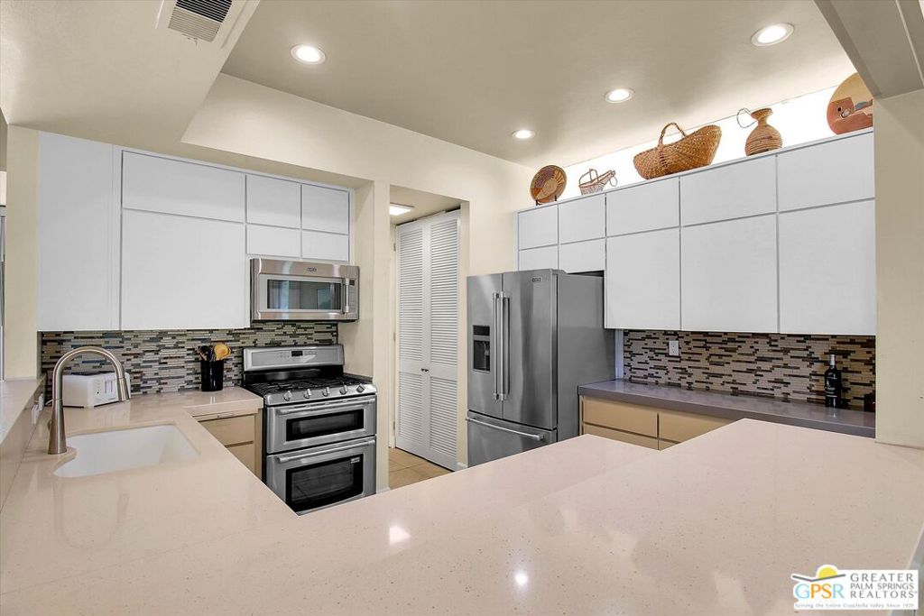 Kitchen with white cabinets, a mosaic backsplash, stainless steel appliances, and a broad pale countertop.