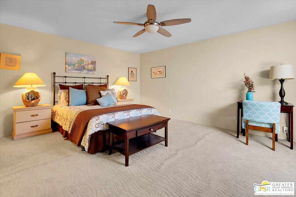 Furnished bedroom with colorful layered bedding, a ceiling fan, and a blue chair.