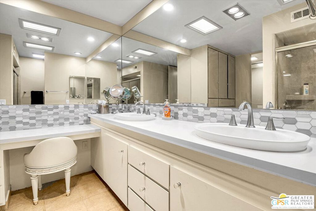 Bathroom with double vessel sinks, a long white vanity, mirrored wall, and gray hexagonal tile backsplash.