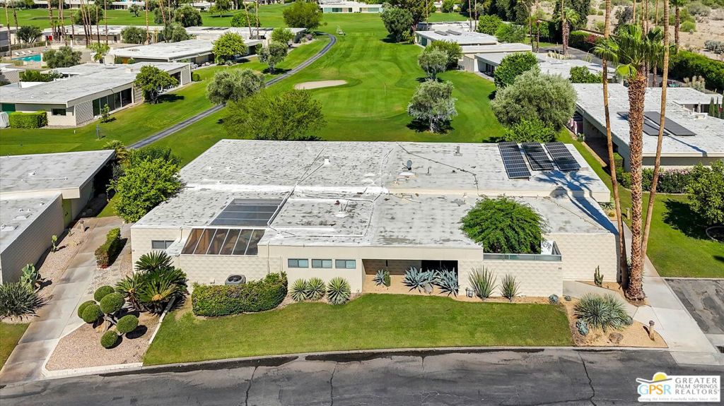 Modern Palm Springs home with rooftop solar panels, landscaped front yard, and golf course behind it.